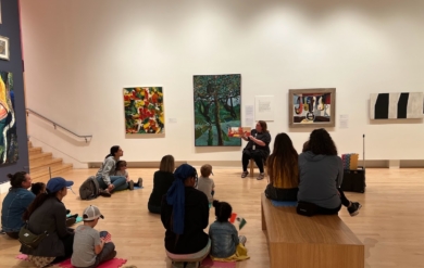 Children sitting in front of art and an educator while being read a story.